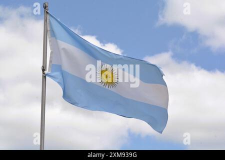 Die Nationalflagge der Argentinischen Republik fliegt an einem schönen Sommertag mit blauem Himmel und weißen Wolken einen Fahnenmast hoch. Stockfoto