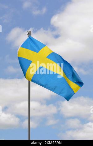 Die Nationalflagge Schwedens fliegt an einem schönen Sommertag mit blauem Himmel und weißen Wolken einen Fahnenmast hoch. Stockfoto