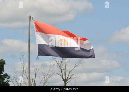 Die Nationalflagge Ägyptens fliegt an einem schönen Sommertag mit blauem Himmel und weißen Wolken einen Fahnenmast hoch. Stockfoto