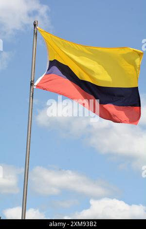 Die Nationalflagge Kolumbiens fliegt an einem schönen Sommertag mit blauem Himmel und weißen Wolken einen Fahnenmast hoch. Stockfoto