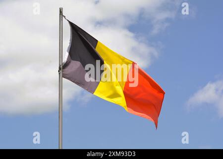 Die belgische Nationalflagge fliegt an einem schönen Sommertag mit blauem Himmel und weißen Wolken einen Fahnenmast hoch. Stockfoto