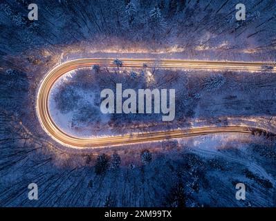 Autoscheinwerfer beleuchten eine winterliche Straße nach Einbruch der Dunkelheit. Lange Belichtungszeit. Transport im Winter bei Nacht. Stockfoto
