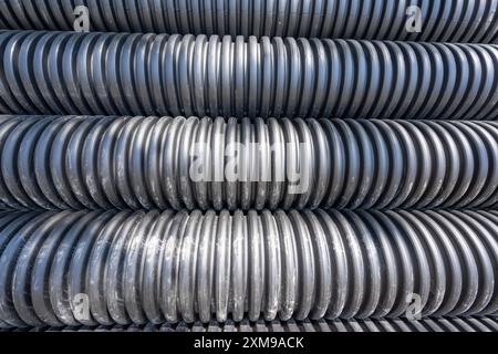 Stapel eines schwarzen HDPE-Kanalrohrs (HDPE-Kunststoff N-12) auf einem Projektstandort, der auf die Installation wartet. Stockfoto