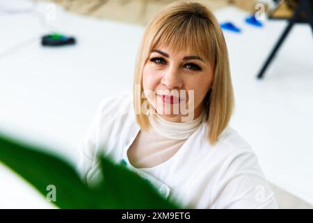 Eine Frau mit blondem Haar und rotem Lippenstift posiert für ein Porträt in einem weißen Raum. Stockfoto