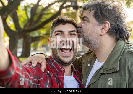 Ein glücklich verheiratetes schwules Paar lächelt und lacht, während es Selfies macht. Stockfoto