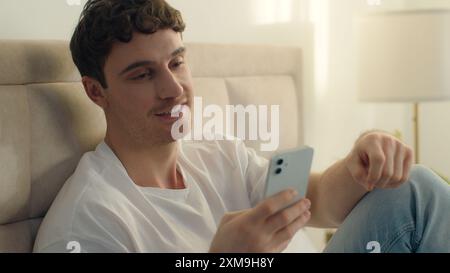 Kaukasischer europäischer Mann männlicher Mann Haus Schlafzimmer mit Handy Smartphone-Technologie kommunizieren Sprechen Video Chat Anruf Lächeln Internet-Verbindung Stockfoto
