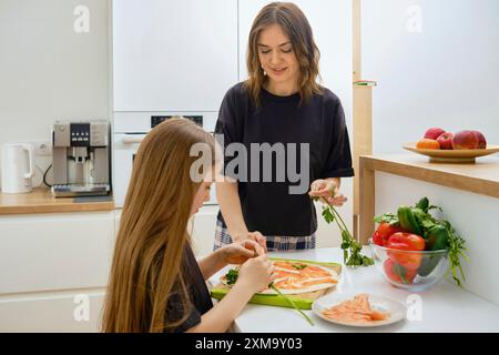 Mutter und kleine Tochter bereiten gemeinsam gesunde Fischvorspeise in der Küche vor Stockfoto