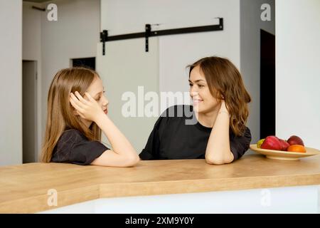 Glückliche Mutter und Tochter sitzen hinter der Küchenzeile Stockfoto