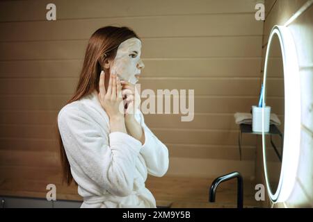 Frau, die vor einem Spiegel eine Maske mit Mineralien auf ihr Gesicht aufträgt Stockfoto