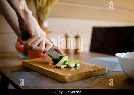 Nahaufnahme einer weiblichen Hand, die Frischgurke mit Messer auf Holzschneidebrett schneidet Stockfoto