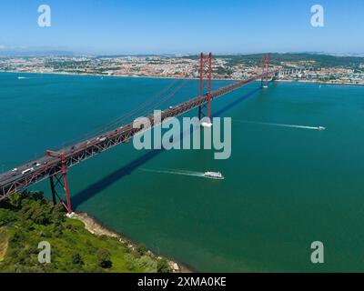 Rote Brücke überspannt das Wasser, gesäumt von Booten, mit einer Stadt und Natur im Hintergrund an einem sonnigen Tag, Blick aus der Luft, Ponte 25 de Abril, Brücke von Stockfoto