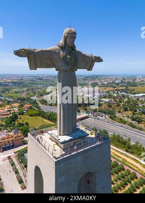 Große Statue von Jesus mit ausgestreckten Armen auf einer Plattform, mit Blick auf die Stadtlandschaft an einem klaren Sommertag, aus der Luft, Statue Cristo Rei, Almada Stockfoto