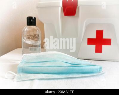 Erste-Hilfe-Set mit rotem Kreuz, Handdesinfektionsmittel und blauer Gesichtsmaske auf weißer Oberfläche Stockfoto