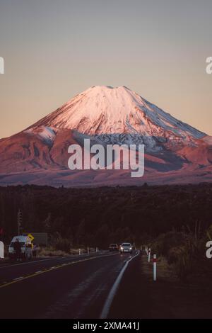 Schneebedeckter Berg im Hintergrund, Straße mit Autos bei Sonnenuntergang, Tongariro Nationalpark, Neuseeland Stockfoto