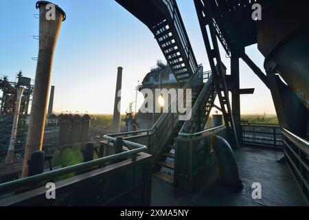 Industrieruine bei Sonnenaufgang mit Treppen, Metallkonstruktionen und Rohren, von warmem Sonnenlicht durchflutet, Landschaftspark Duisburg Nord, Meiderich Huette Stockfoto