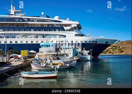 Ein großes Kreuzfahrtschiff im Hafen einer griechischen Insel, umgeben von kleineren Fischerbooten auf blauem Wasser, Skala, Patmos, Dodekanes, Griechisch Stockfoto