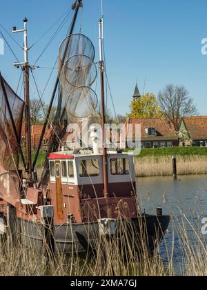 Ein Boot mit einem Fischernetz im Wasser mit kleinen Häusern im Hintergrund unter klarem Himmel, enkhuizen, niederlande Stockfoto