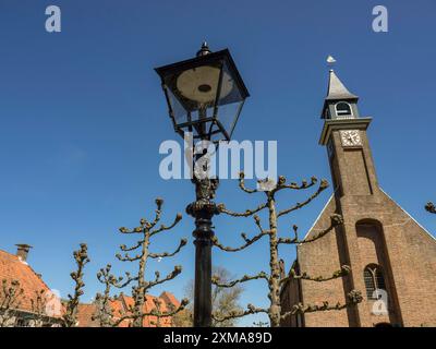 Historische Dorfkirche mit einem alten Kirchturm unter blauem Himmel und gepflegten Bäumen, enkhuizen, niederlande Stockfoto