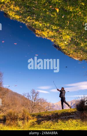 Männlicher Golfer reflektierte sich in einem Wasserteich und schlug den Golfball auf dem Fairway auf dem Golfplatz mit Mountain an einem sonnigen Tag in der Schweiz Stockfoto