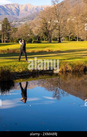 Männlicher Golfer reflektierte sich in einem Wasserteich und schlug den Golfball auf dem Fairway auf dem Golfplatz mit Mountain an einem sonnigen Tag in der Schweiz Stockfoto