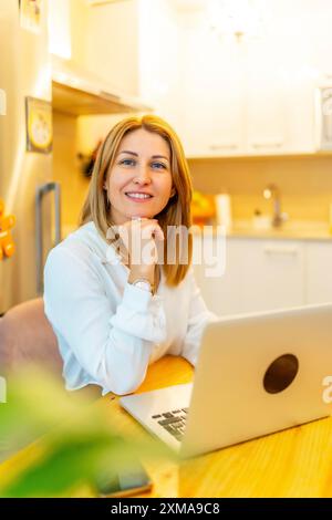 Vertikales Porträt einer eleganten blonden Frau, die von zu Hause aus mit dem Laptop arbeitet Stockfoto