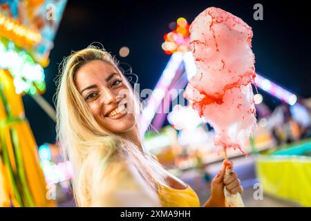 Eine blonde Frau macht Selfie mit rosa Zuckerwatte in einem Vergnügungspark Stockfoto