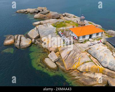 Ein Leuchtturm auf einer felsigen Insel, umgeben von klarem Wasser, mit einem orangen Dach und einem kleinen Gebäude, mit Blick aus der Luft, Eine Illa de Arousa, La Isla Stockfoto