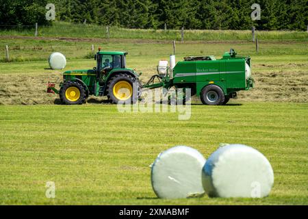 Heuernte, Landwirt mit Landmaschine, nimmt gemähtes Heu auf, das sofort zu Ballen gepresst und in Folie, Ballenpresse/Wickler, gewickelt wird Stockfoto