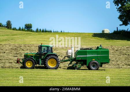 Heuernte, Landwirt mit Landmaschine, nimmt gemähtes Heu auf, das sofort zu Ballen gepresst und in Folie, Ballenpresse/Wickler, gewickelt wird Stockfoto