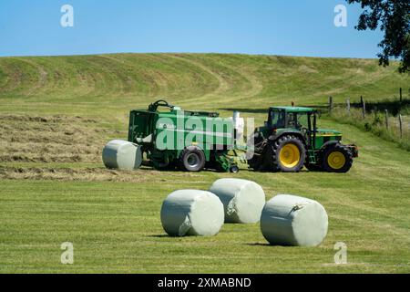 Heuernte, Landwirt mit Landmaschine, nimmt gemähtes Heu auf, das sofort zu Ballen gepresst und in Folie, Ballenpresse/Wickler, gewickelt wird Stockfoto