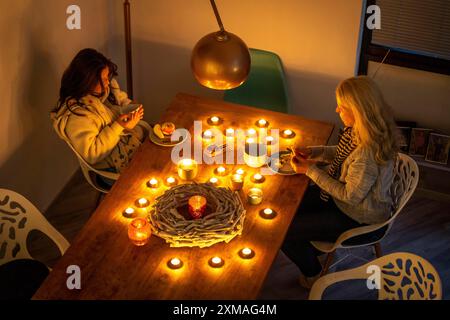 Symbolisches Bild Energiesparen, kalter Winter, Energiekrise, kalte Wohnung, Mutter und Tochter beim Abendessen warm gekleidet, nur bei Kerzenschein, Heizung auf Stockfoto