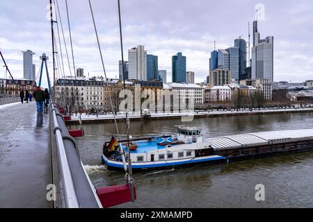 Winter in Frankfurt, Blick auf die Skyline des Stadtzentrums, von der Holbeinsteg Fuß- und Radbrücke, Frachter auf dem schneebedeckten Main Stockfoto