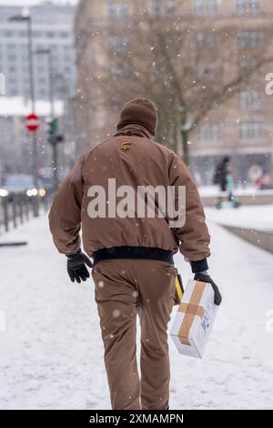 Winter in Frankfurt bringt UPS Mitarbeiter ein Paket zu Fuß zu einem Kunden, da das Winterwetter im Bankenviertel Hessen herrscht Stockfoto