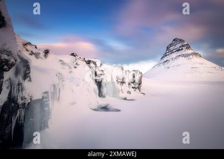 Farbenfroher Sonnenaufgang am Mount Kirkjufell, wunderschöne Aussicht mit dem gefrorenen Wasserfall im Vordergrund, Winteraufnahme Stockfoto