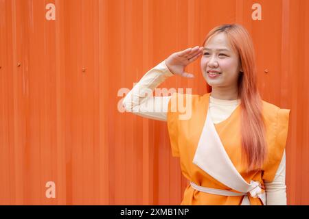 Porträt einer schönen asiatischen Frau, die vor orangefarbenem Hintergrund grüßt und lächelt Stockfoto