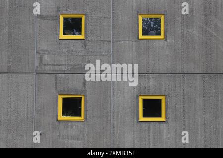 Vier gelb gerahmte kleine Fenster in einer Betonmauer. Stockfoto