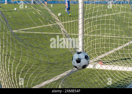 Ein schwarz-weißer Fußball, der durch einen kräftigen Schuss angetrieben wird und das Netz durchbricht, um ein perfektes Tor zu erzielen. Das wulstige Netz betont den Aufprall und die Qualität Stockfoto