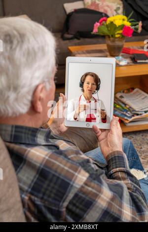 Symbolisches Bild der Telemedizin, älterer Patient, der in einer Videokonferenz von zu Hause aus mit einem Arzt spricht Stockfoto