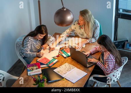 Während der Abriegelung im Januar 2021 hilft Mutter ihren beiden Töchtern zu Hause beim Lernen, mit Lehrbüchern und Computern, Schulschließungen Stockfoto