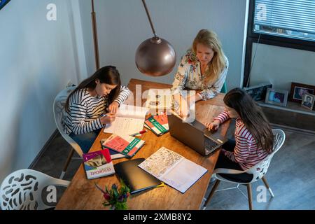 Während der Abriegelung im Januar 2021 hilft Mutter ihren beiden Töchtern zu Hause beim Lernen, mit Lehrbüchern und Computern, Schulschließungen Stockfoto