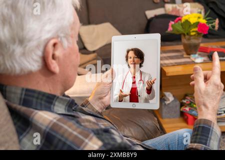 Symbolisches Bild der Telemedizin, älterer Patient, der in einer Videokonferenz von zu Hause aus mit einem Arzt spricht Stockfoto