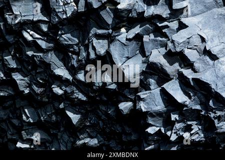 Das Bild ist eine Nahaufnahme einer Felswand mit einem schwarz-grauen Farbschema. Die Felsen sind zerklüftet und rau, was den Eindruck eines rauen und zerklüfteten Gesteins vermittelt Stockfoto