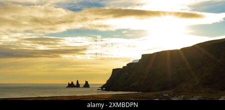 Die Sonne untergeht über dem Meer und strahlt ein warmes Licht auf das felsige Ufer. Der Himmel ist voller Wolken, die eine ruhige und friedliche Atmosphäre schaffen. V Stockfoto