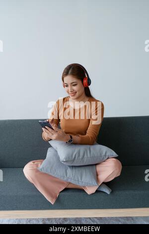 Eine Frau fühlt sich völlig entspannt, während sie mit ihren Kopfhörern sitzt und Musik auf ihrem Smartphone hört. Stockfoto