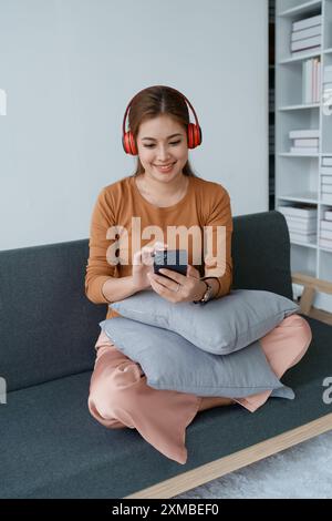 Eine Frau fühlt sich völlig entspannt, während sie mit ihren Kopfhörern sitzt und Musik auf ihrem Smartphone hört. Stockfoto