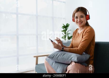 Eine Frau fühlt sich völlig entspannt, während sie mit ihren Kopfhörern sitzt und Musik auf ihrem Smartphone hört. Stockfoto