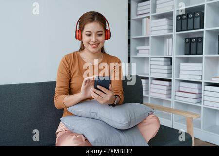 Eine Frau fühlt sich völlig entspannt, während sie mit ihren Kopfhörern sitzt und Musik auf ihrem Smartphone hört. Stockfoto