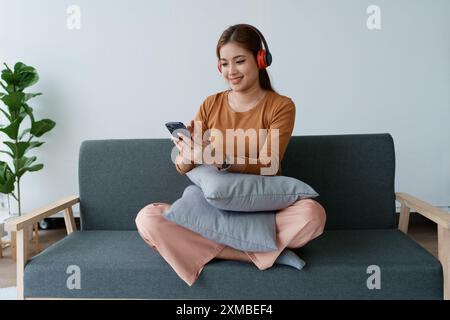 Eine Frau fühlt sich völlig entspannt, während sie mit ihren Kopfhörern sitzt und Musik auf ihrem Smartphone hört. Stockfoto