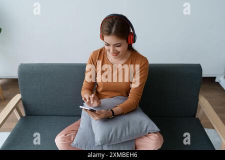 Eine Frau fühlt sich völlig entspannt, während sie mit ihren Kopfhörern sitzt und Musik auf ihrem Smartphone hört. Stockfoto