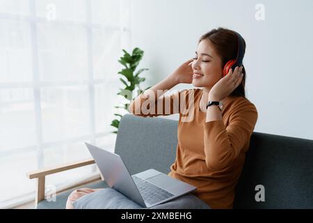 Eine Frau fühlt sich völlig entspannt, während sie mit ihren Kopfhörern sitzt und Musik auf ihrem Laptop hört. Stockfoto